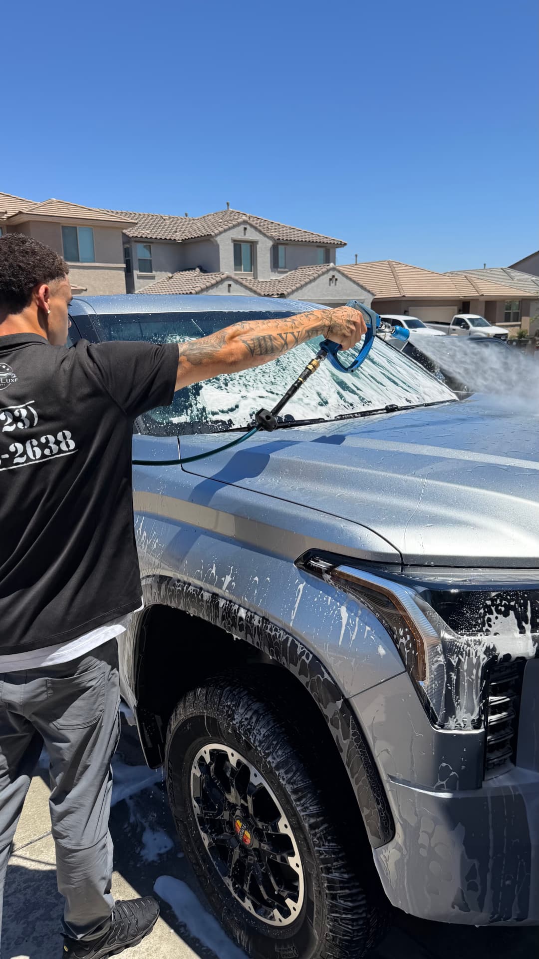 Detailer foam-washing a silver Toyota Tundra in a residential driveway